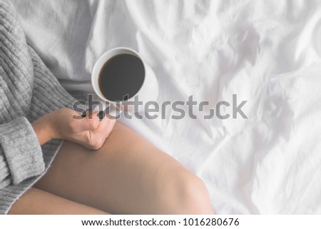 girl in bed wearing wool sweater holding cup of coffee