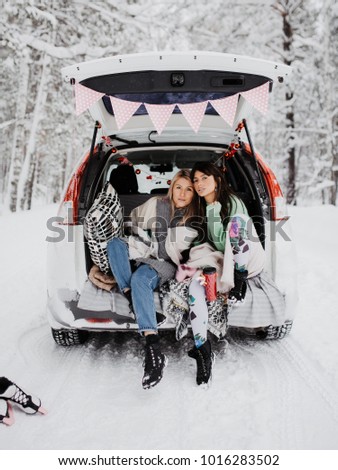 Two friends making a stop in winter forest, sitting in trunk of their car.