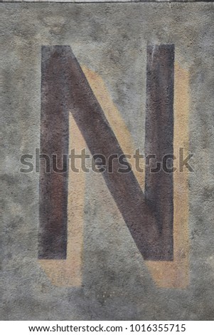 Capital letter N written on a grey ancient wall. Dark painted character on a flat vertical surface. Simple abstract picture. Isolated symbol of the alphabet. Brown, black, grey and beige colors.  