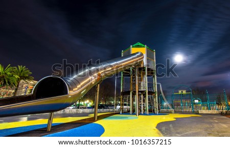 Toboggan for kids from a low perspective. Colorfull long exposure picture of the playground at night time, with full moon and cloud trails in the sky, side view.