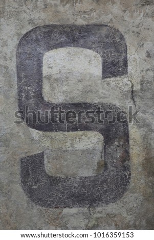 Capital letter S written on a grey ancient wall. Dark painted character on a flat vertical surface. Simple abstract picture. Isolated symbol of the alphabet. Brown, black, grey and beige colors.  