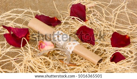 A wrapper of paper lies on the sisal. Scroll on a background of dry rose petals. The concept of a love message. Valentine's Day. Horizontal image.
