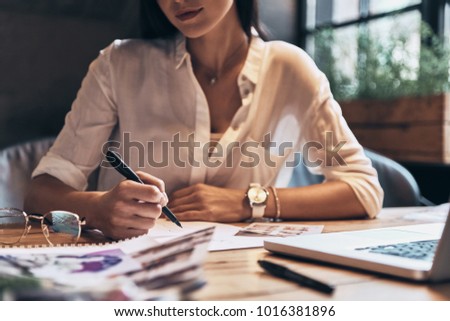 Close up of young woman working on sketches while sitting in her workshop          