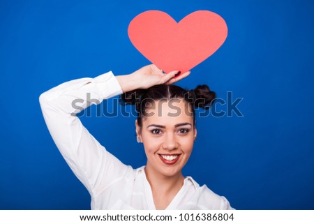 Pretty woman holding a red papper heart on blue background in studio photo