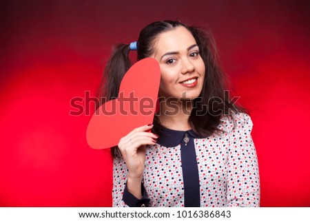 Portrait of happy woman holding a papper heart in hands on dark red background