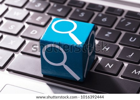 Close-up Of Magnifying Glass Symbol On Blue Wooden Block Over The Laptop Keypad