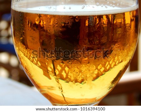 Would you like to have a beer? A portrait of a glass of beer with foam, reflection of the surroundings