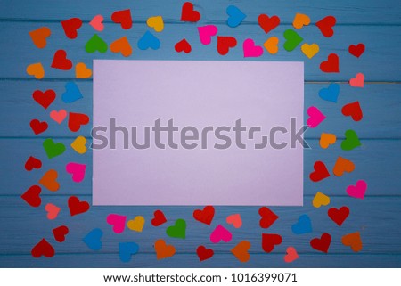 White blank of paper with multicolored hearts around on blue wooden background. Love background. Love concept