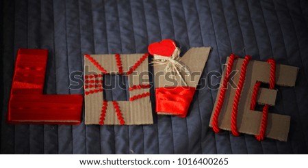 handmade cardboard love sign with red ribbons and heart on the bed cover