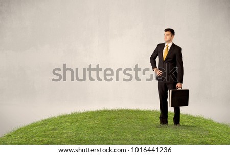 A successful caucasian elegant business man standing in small green grass with briefcase in front of clear empty background concept.