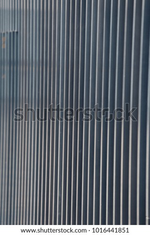 Close up view of an iron protection gate made of flat bars. Color nuances between blue and grey. Design with vertical and parallel lines. Patterns of bright streaks in perspective. Urban modern photo 