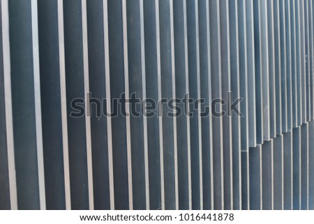 Close up view of an iron protection gate made of flat bars. Color nuances between blue and grey. Design with vertical and parallel lines. Patterns of bright streaks in perspective. Urban modern photo 