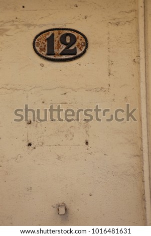 Close up view of the number 12 written on an oval metallic plate on the exterior wall of a house. Numeric element fixed on a beige stone wall. Old texture. Simple image taken in a street in France.