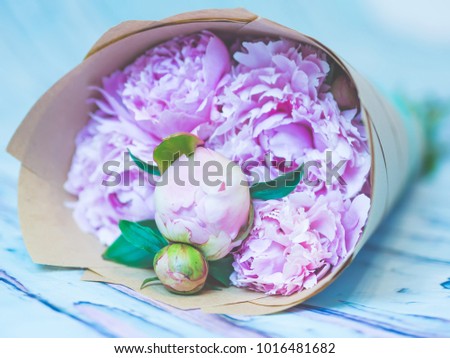 A bouquet of beautiful pink peonies on a bluish rustic wooden table shot against soft-focused background.