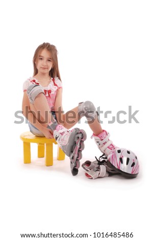 Charming broun-haired girl of school age in short jeans shorts and a pink t-shirt sitting on the chair and tries to foot roller skates. Isolated on white background