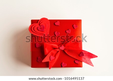 A red cardboard gift box tied with a red bow and adorned with hearts on the white background.Concept is of special days.