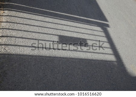 Close up view of the shadow of a wall equiped with a mettalic closed gate. Silhouette of the door reflected on the grey floor. Stripes on the surface. Abstract picture of a building element. 