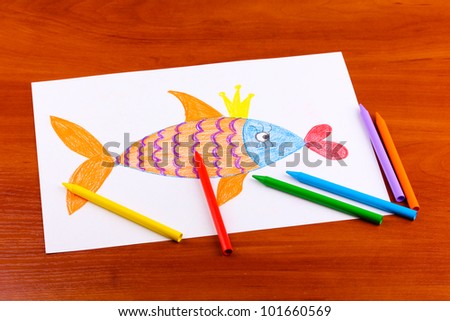 Children's drawing of golden fish and pencils on wooden background