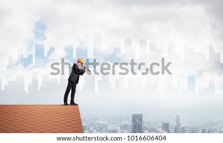 Young businessman in suit and helmet on roof edge. Mixed media