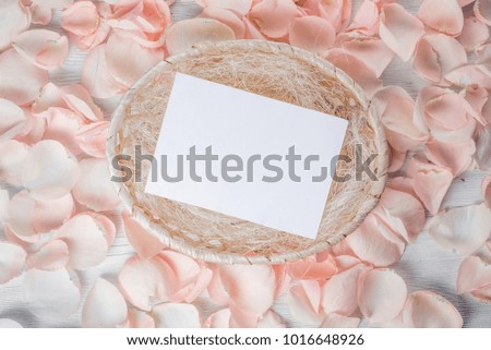 petals of roses on a white table background with a basket and white sheet for text