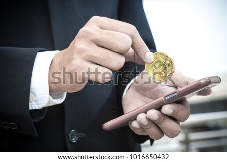 man wearing business suit holding Gold Bitcoin from mobile phone, transfer money concept