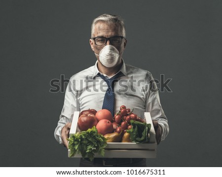 Businessman with protective mask holding a crate with polluted poisonus vegetables, food pollution concept Royalty-Free Stock Photo #1016675311