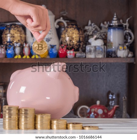 Girl's hand holding bitcoin replica over a piggy bank
