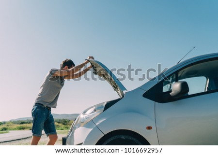 Young man looking under the hood of breakdown car outdoors. Transportation and vehicle concept Royalty-Free Stock Photo #1016692957
