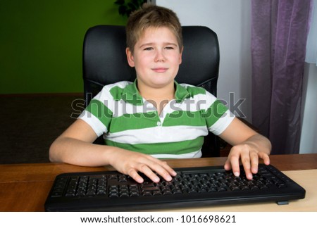 Obese little boy sitting at the computer.