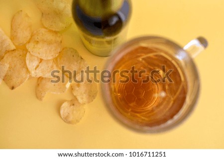 glass mug with beer and a picture of a soccer ball and chips on a yellow background. The view from the top.