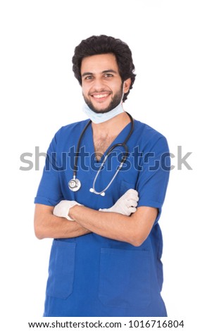 A standing young surgeon wearing gloves and blue uniform, crossed arms, isolated on a white background.