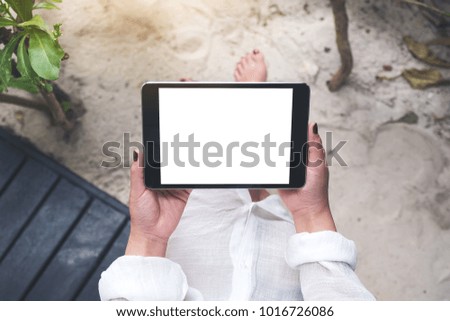 Mockup image of a woman's hand holding black tablet pc with blank white desktop screen with sand and beach background