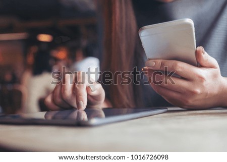 Closeup image of a woman's hand pointing and touching tablet pc while using mobile phone in cafe