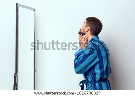 man in a bathrobe looks in a mirror on a light background                              