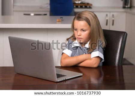 young beautiful sweet little girl 6 to 8 years old with blond hair and blue eyes sitting at home kitchen enjoying with laptop computer concentrated watching internet cartoon movie in lifestyle concept