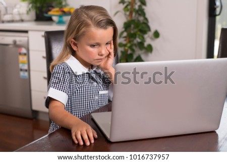 young beautiful sweet little girl 6 to 8 years old with blond hair and blue eyes sitting at home kitchen enjoying with laptop computer concentrated watching internet cartoon movie in lifestyle concept