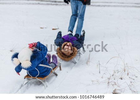 Happy family rides the sledge in the winter wood or forest, cheerful entertainments, everything is covered with snow around. small boy and girl in the park outdoors playing with  snow. happy childhood