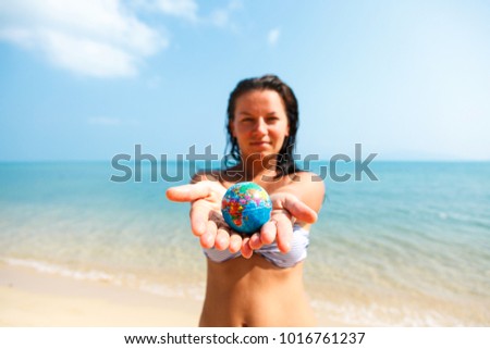 A girl in a swimsuit holds a globe in her arms, stretched forward, against the background of the Pacific Ocean