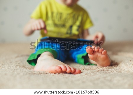 Little cute boy in a green T-shirt playing games on a tablet and watching cartoons. Focus on feet