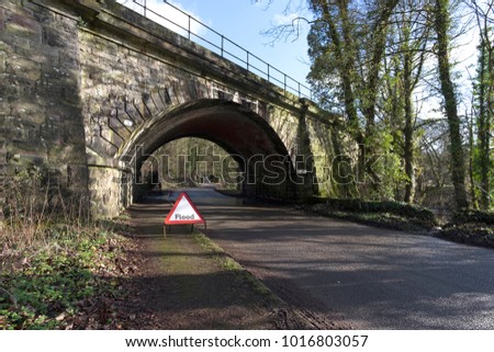 Flood warning triangle road sign in front of a railway bridge tunnel