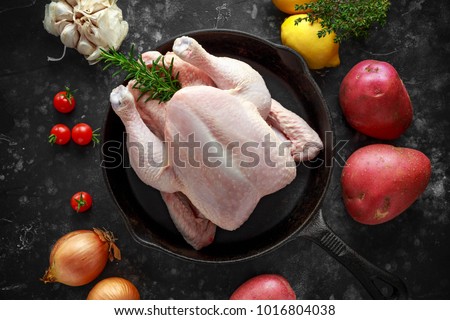 Whole raw Free range chicken in rustic skillet with rosemary leaf, thyme, lemon, red potatoes and garlic. ready to cook Royalty-Free Stock Photo #1016804038
