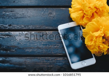 Mobile with black screen, can add texts or picture, top view on wood table with yellow flower