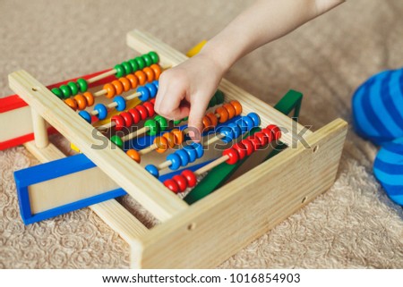 Hand of little boy playing with abacus. Clouse up picture of curly cute toddler playing with wooden toy. Children education. Preschooler baby learns to count.