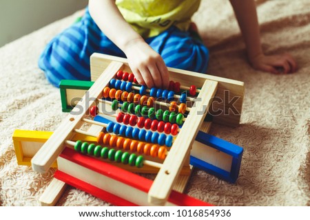 Hand of little boy playing with abacus. Clouse up picture of curly cute toddler playing with wooden toy. Children education. Preschooler baby learns to count.