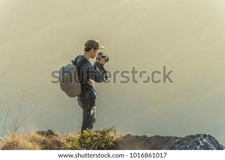 Photographer with camera in hand on top of mountain. Hiker climbed on peak of rock above foggy valley.
