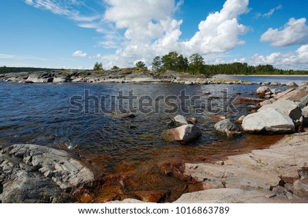 Summer landscape. The stone coast of the bay, the stone isthmus, stones in clear water, pine on the stones. Blue sky and white clouds. Russia, Finland, Karelia, Lake Ladoga