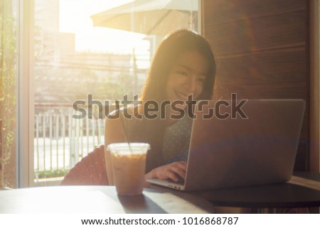 Portrait of cute asian teen woman using a laptops or notebook computer in coffee cafe. morning or sunset moment. selective focus. filtered image and light effect added. happy smile chill out concept