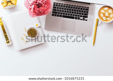 A feminine desktop flat lay hero image,  laptop, pink peony, white planner, and gold stationery accessories. Negative space to the bottom, on a plain white desk background.