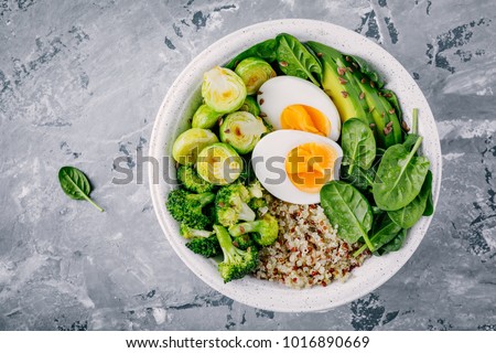 Healthy green vegetarian buddha bowl lunch with eggs, quinoa, spinach, avocado, grilled brussels sprouts and broccoli on dark gray background. Top view.