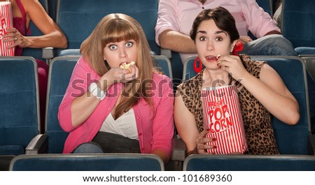 Two amazed women eating popcorn in a theater